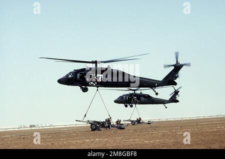 Members of C Btry., 1ST Bn., 319th Air Field Arty. Regt., secure M-102 105mm towed howitzers to the slings of 2nd Battalion, 82nd Aviation Brigade UH-60 Black Hawk (Blackhawk) helicopters for a two-gun raid training mission during Operation Desert Shield. Subject Operation/Series: DESERT SHIELD Country: Saudi Arabia(SAU) Stock Photo