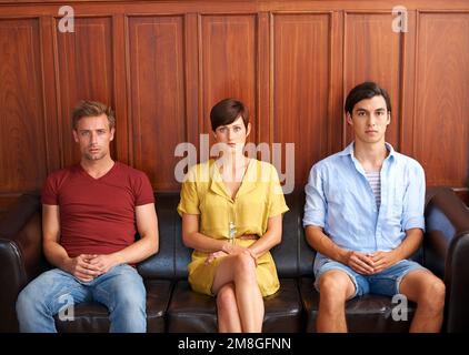 Weve been waiting a long time. Portrait of three young people dressed formally and sitting on a sofa. Stock Photo