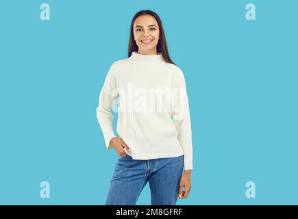 Portrait of beautiful happy young brunette dressed in knitted white sweater and blue jeans, looking at camera. Stock Photo