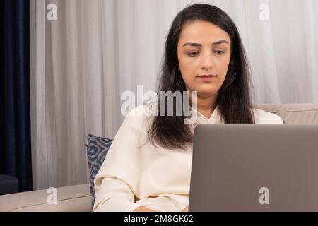 Caucasian woman sitting home and using modern laptop. Freelance employee at living room trying to get finish the project. Female coder or copywriter. Stock Photo