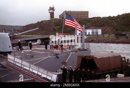 Russian sailors stand in formation on the pier as crew members raise the flag aboard the guided missile cruiser USS YORKTOWN (CG-48) following the vessel's arrival in port. The YORKTOWN and the destroyer USS O'BANNON (DD-987) are visiting Severomorsk as part of an ongoing exchange between the navies of the United States and the Commonwealth of Independent States. The building atop the hill is the headquarters of Northern Fleet. Base: Severomorsk Naval Base Country: Russia (RUS) Stock Photo