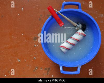 repair work background with a blue plastic basin filled with thick wallpaper glue and a paint round black brush and a red and white roller Stock Photo