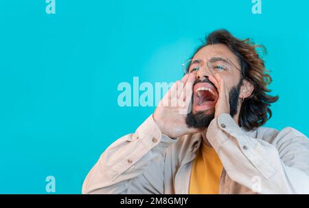 Man shouting loud calling attention with hands like megaphone isolated on blue studio background Stock Photo