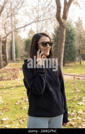 Woman talking on the phone at park, smiling millennial caucasian woman talking on the phone at park. Happy young female holding smartphone. Stock Photo