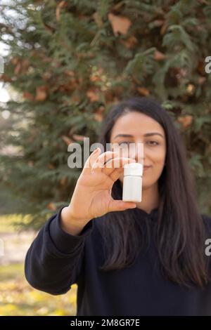 Woman holding empty white pills bottle mock up. Medicine doctor or pharmacist standing outdoor holding and showing pharmaceutical vial. Medical care. Stock Photo