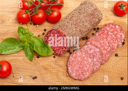 Salami sausage on a wooden board decorated with tomatoes and basil top view Stock Photo