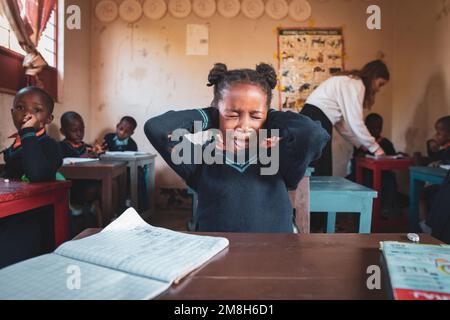 22.05.2022 Mwanza, Tanzania - Girl holds hands on her ears and screams while sitting at her school desk in rural school in Africa Stock Photo