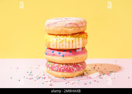 Parchment with different delicious donuts on pink table near yellow wall Stock Photo