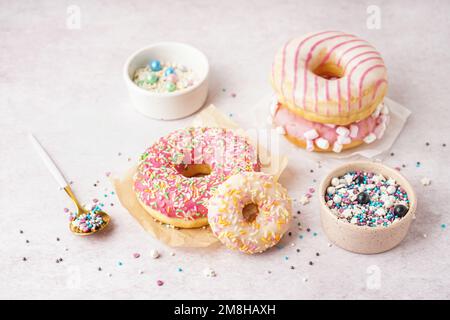 Parchments with different delicious donuts and bowls of sprinkles on white table Stock Photo