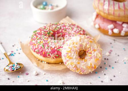 Parchments with different delicious donuts and bowls of sprinkles on white table Stock Photo