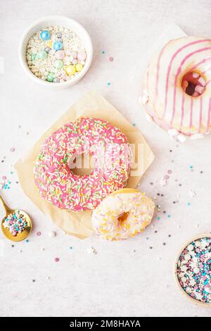 Parchments with different delicious donuts and bowls of sprinkles on white table Stock Photo