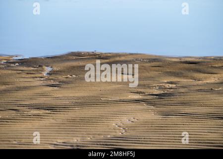 ripples in the sand on a beach near a puddle of water Stock Photo