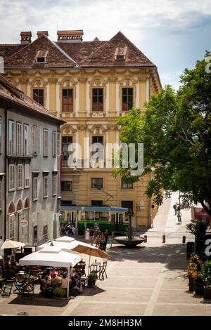 View of Schlossbergplatz i  Graz, Austria as seen from the footpath up to Schlossberg, with restaurants, diners and tram on a summer day Stock Photo