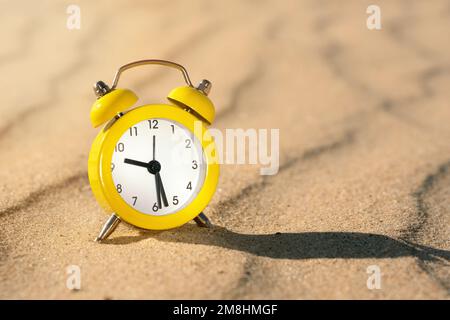 Yellow alarm clock on the sand in the desert on a sunny day with a shadow Stock Photo