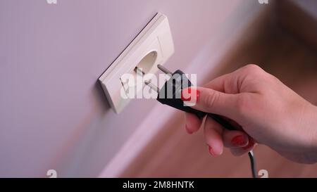 Closeup of woman holding in hand inserts plug into socket Stock Photo