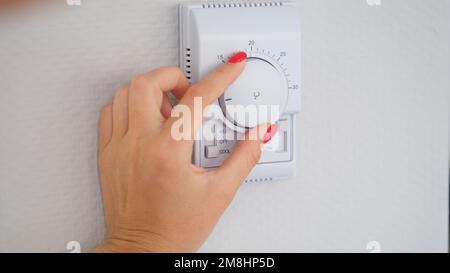 Woman hand adjusts or turns on wall temperature controller controller button Stock Photo