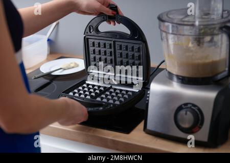 Woman opens waffle iron to make waffles in kitchen. Stock Photo