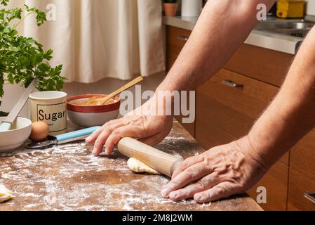 Man's hands with a rolling pin preparing a puff pastry dough in a home kitchen. Stock Photo