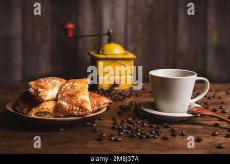 Puff pastry sweets filled with angel hair next to a cup of coffee, with coffee beans scattered on the table and a coffee grinder. Stock Photo