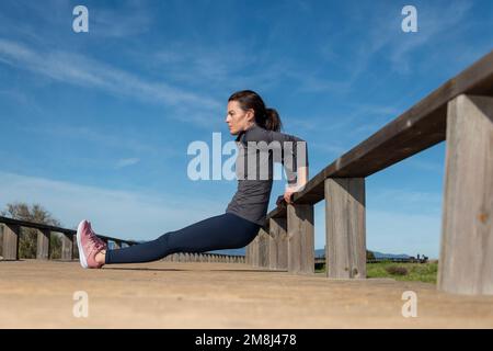 Sporty woman doing reverse push ups outside on a wooden railing. Stock Photo