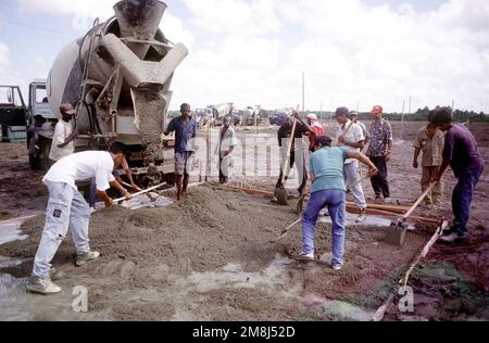 Surinam construction workers spread concrete that is being poured from a mixer truck for a floor in the Haitian migrant camp. A line of mixer trucks can be seen in the background ready to deliver their load.(Exact date unknown). Subject Operation/Series: DISTANT HAVEN Country: Suriname (SUR) Stock Photo