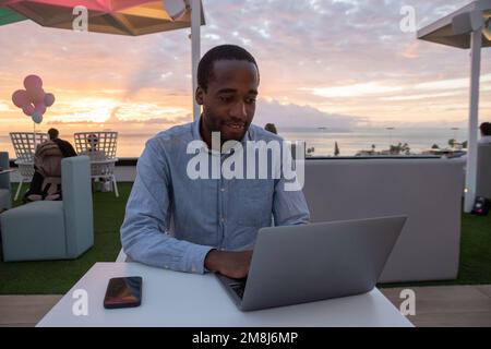 Young businessman working on his laptop with a beautiful sunset over the ocean in the background Stock Photo
