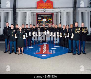 Exterior, MLS, MG Charles E. Wilhelm, USMC, Commanding General 1ST Marine Division and 18 members of his principal staff, in dress blues and holding hats, line up on two sides of a large replica of the 1ST Marine Division Patch and Seal. In background behind the staff is a sign, 'HEADQUARTERS 1ST MARINE DIVISION (REIN) FLEET MARINE FORCE'. Behind the staff is a large plaque showing the 1ST marine Division's Decorations and a ship's bell. The bell is from the USS WHARTON (AP-7) a WW II Troop Transport. The ship was named for the third Commandant of the Marine Corps, LTC Frank Wharton. Base: Mar Stock Photo