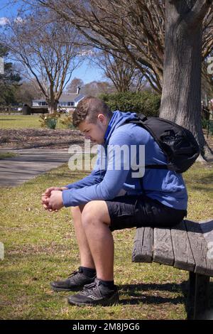 Teenage Boy sitting on a bench outside thinking.  Contemplative. Sad. Stock Photo