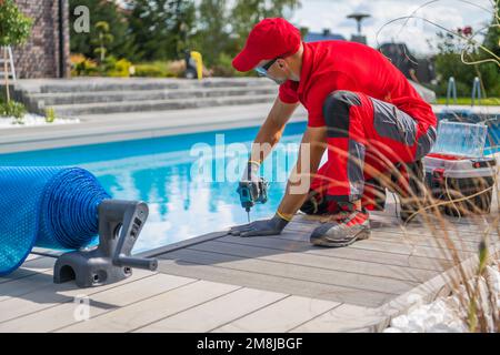 Residential Backyard Swimming Pool Deck Building. Poolside Deck Made From a Modern Composite Panels. Caucasian Worker in His 40s. Stock Photo