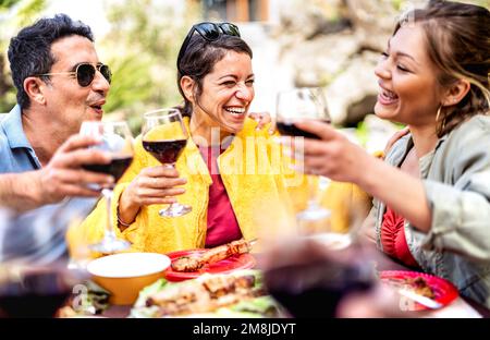 Happy friends on genuine mood drinking red wine at pic nic party - Mixed age range people having fun together at restaurant winery patio out side Stock Photo