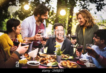 Young men and women having fun drinking out at wine diner - Food and beverage life style concept on mixed age people enjoying time together at villa Stock Photo