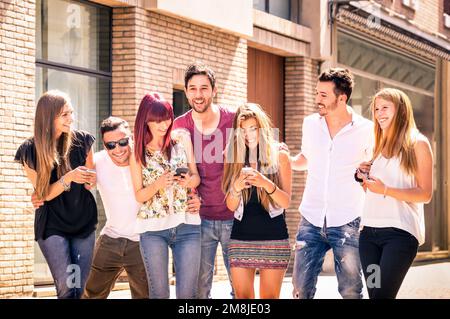Group of young best friends having fun together walking on town street - Moment of technology interaction in everyday lifestyle - Internet connection Stock Photo