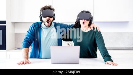 Millennial couplr playing with vr glasses at home kitchen - Virtual reality and tech concept with engaged people having fun throug headset goggle Stock Photo