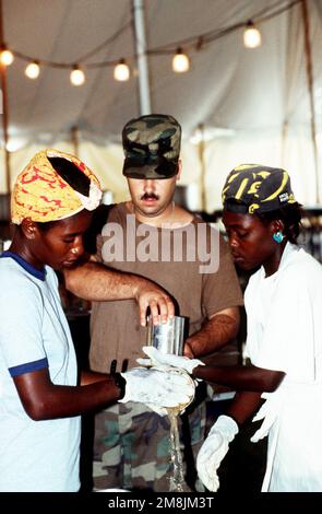 SPC. Phillips, US Army, Hunter Army Airfield, Fort Stewart, GA, helps prepare meals with Haitian refugees that have volunteered to cook in the mess tent at McCallah Field. Subject Operation/Series: SEA SIGNAL Base: Guantanamo Bay Country: Cuba (CUB) Stock Photo