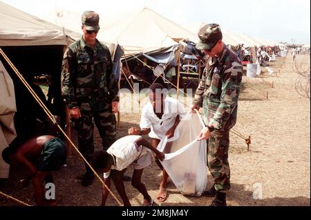 AIRMAN 1ST Class Jeff Leyshon (left) and Samuel Crow (right) from the 2nd Security Police Squadron (SPS), Barksdale, LA, help Haitians with the cleanup of their Camp. Subject Operation/Series: SEA SIGNAL Base: Guantanamo Bay Country: Cuba (CUB) Stock Photo