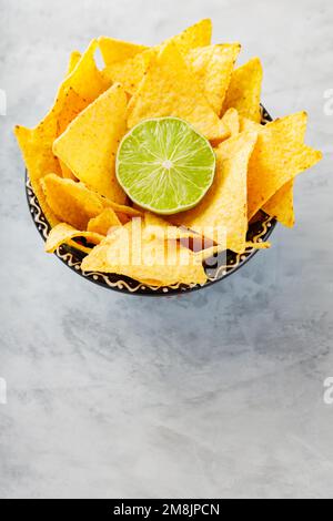 Nachos tortilla chips in a bowl. Bowl of corn tortilla chips and lime on concrete. Top view. Copy space Stock Photo