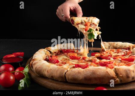 margarita pizza. A man's hand takes a slice of pizza with a spatula, the cheese on the pizza stretches Stock Photo