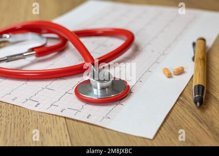 close-up of red stethoscope on electrocardiogram (ECG) paper, on the right pills and a bamboo pen Stock Photo