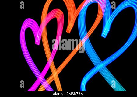 Hand made light painting of three hearts in pink, red and blue on black backdrop Stock Photo