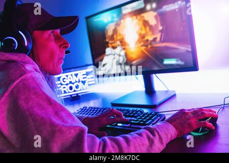 Professional Female Gamer Playing in First-Person Shooter Online Video Game on her Personal Computer. Room Lit by Neon Lights in Retro Arcade Style. Stock Photo