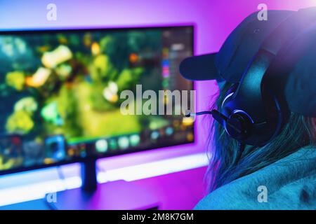 female Gamer plays strategy Online Video Game on her Personal Computer. Room Lit by Neon Lights in Retro Arcade Style. Online Cyber e-Sport Internet Stock Photo