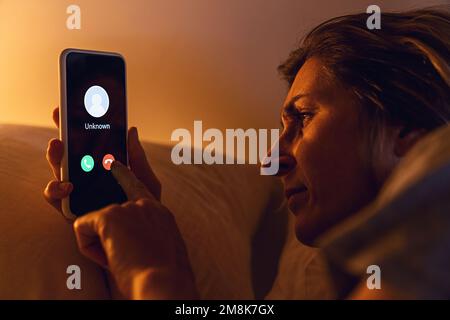 Unknown caller calling in the middle of the night. Phone call from stranger. Woman holding smartphone in bad late. Unexpected call disturbs at night Stock Photo