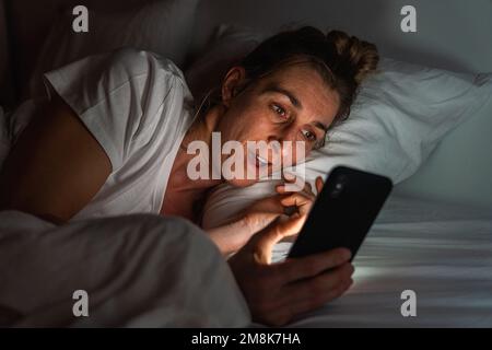 Woman using smartphone late at night in bed. Person looking at Online dating app photos from man with cell in dark home. Sexting or cheating concept Stock Photo