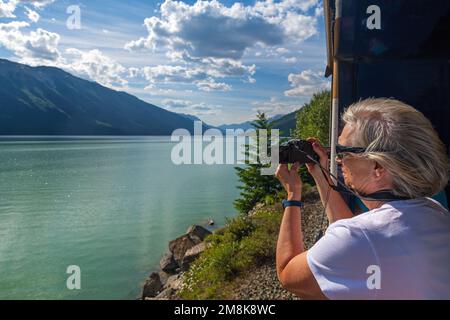 Female tourist taking photographs of Moose Lake in gold leaf wagon of Rocky Mountaineer train in Jasper national park, Canada. Stock Photo