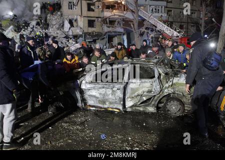 DNIPRO, UKRAINE - JANUARY 14, 2023 - Men remove one of the cars that caught fire after a rocket launched by Russian occupiers during a massive missile attack on Ukraine earlier Saturday hit an apartment block, Dnipro, central Ukraine. As reported, 10 people, including a 15-year-old girl, were killed. Credit: Ukrinform/Alamy Live News Stock Photo