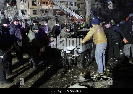 DNIPRO, UKRAINE - JANUARY 14, 2023 - Men remove one of the cars that caught fire after a rocket launched by Russian occupiers during a massive missile attack on Ukraine earlier Saturday hit an apartment block, Dnipro, central Ukraine. As reported, 10 people, including a 15-year-old girl, were killed. Credit: Ukrinform/Alamy Live News Stock Photo