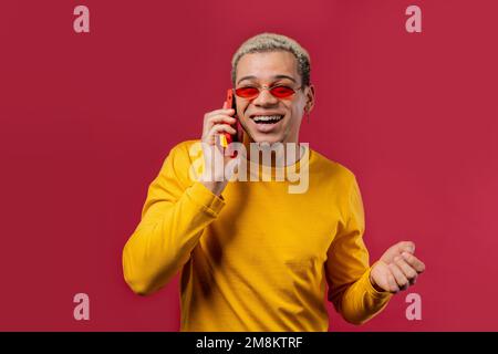 Stylish man talking by phone, nice joke, smiling. Young guy on red background. Having smartphone call.  Stock Photo