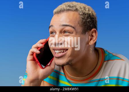 Smiling positive man talking by phone, nice joke, smiling. Young guy on blue background. Having smartphone call.  Stock Photo