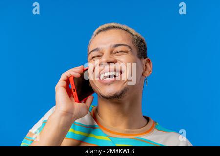 Smiling positive man talking by phone, nice joke, smiling. Young guy on blue background. Having smartphone call.  Stock Photo