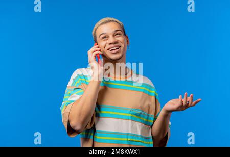 Smiling positive man talking by phone, nice joke, smiling. Young guy on blue background. Having smartphone call.  Stock Photo